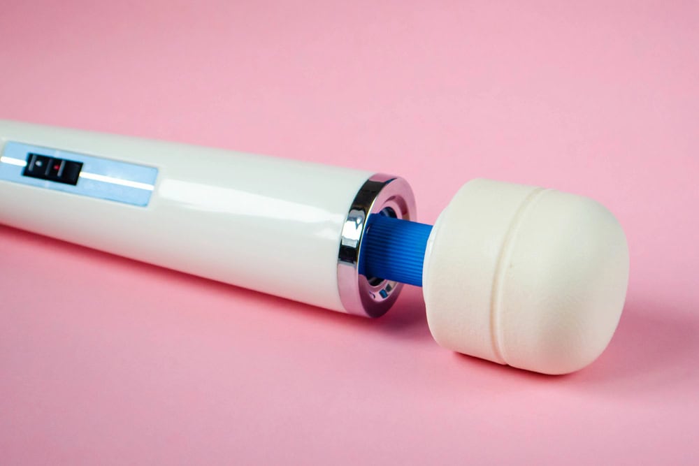 A white handheld electric massager with a large rounded head, lying on a pink surface, makes an ideal hotwife bedroom toy for luxurious relaxation and intimate moments.