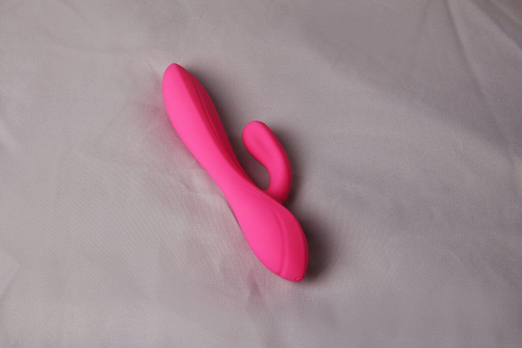A pink silicone dual-ended vibrator, perfect as a hotwife vibrator, rests elegantly on a light gray fabric surface.