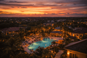 A sunset view of Secrets Hideaway Orlando’s resort pool, surrounded by palm trees, lounge chairs, and people, with buildings and distant city lights in the background-a premier swinger resort near me.